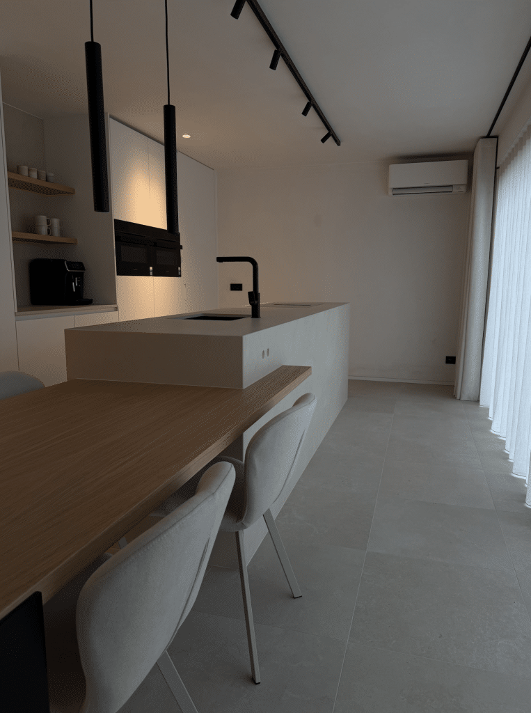 Interieurfoto van een moderne open keuken met licht kookeiland, houten tafel, witte stoelen en zwarte hanglampen in een lichte nieuwbouw woonkamer