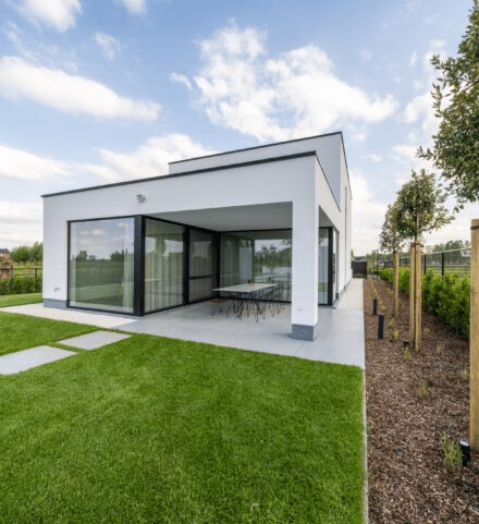 Achteraanzicht van een moderne witte nieuwbouwwoning met een overdekt terras, grote raampartijen en een strak aangelegde tuin met gazon