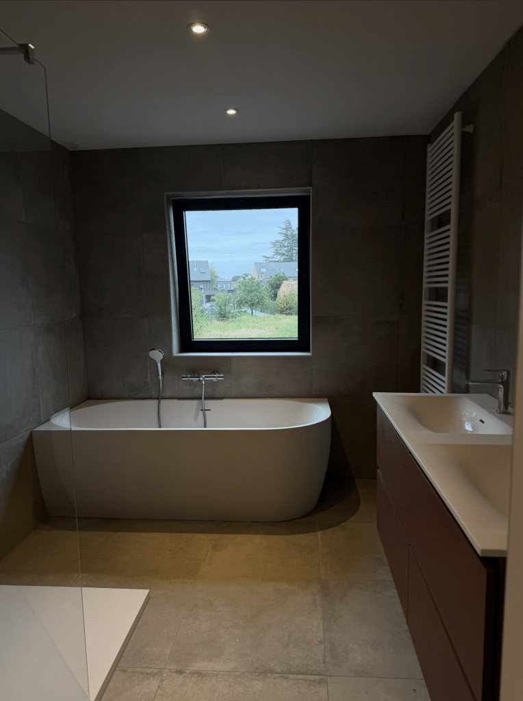 Moderne, strak afgewerkte nieuwbouw badkamer met vrijstaand bad, houten meubel, dubbele wastafel en inloopdouche, als voorbeeld van een hoogwaardige afwerkingsgraad