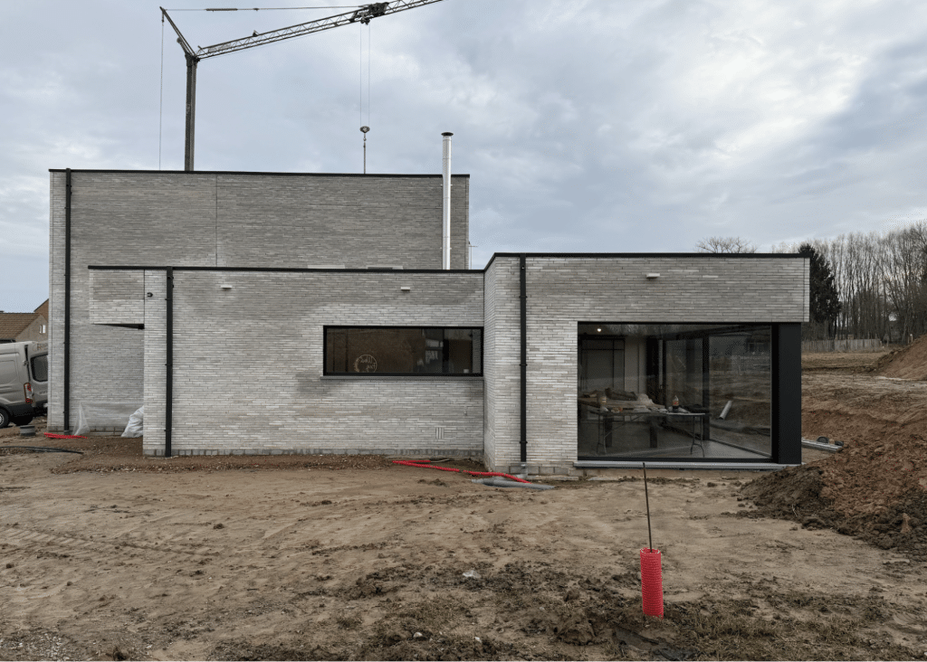 Moderne nieuwbouwwoning in opbouw met lichte gevelsteen en grote raampartijen.