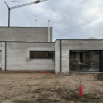 Moderne nieuwbouwwoning in opbouw met lichte gevelsteen en grote raampartijen.