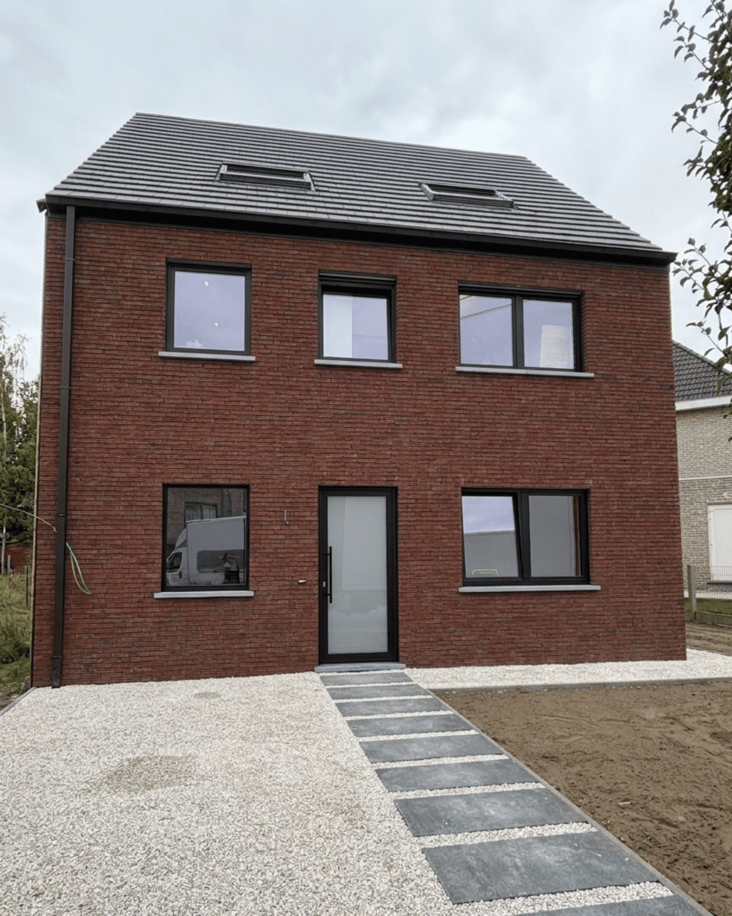 Afgewerkte nieuwbouwwoning in rode baksteen met zwarte raamprofielen en een strakke grindoprit.
