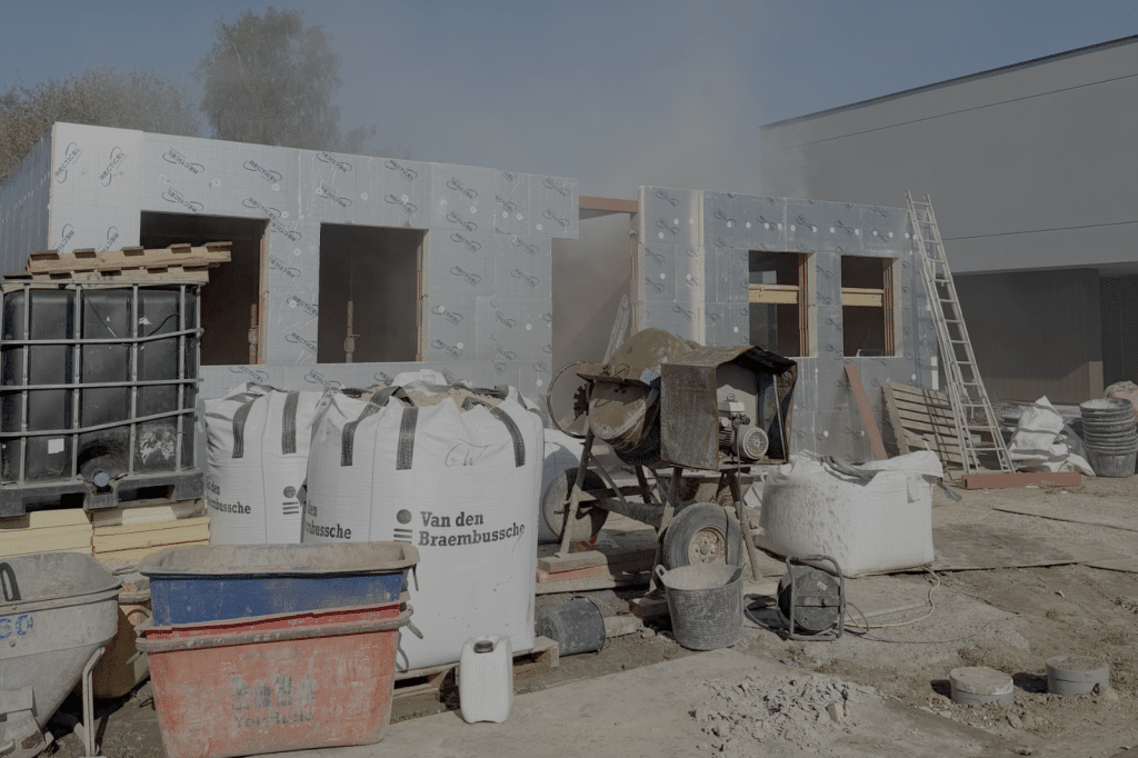 Actieve bouwwerf met isolatiepanelen, een betonmixer en bouwmaterialen.
