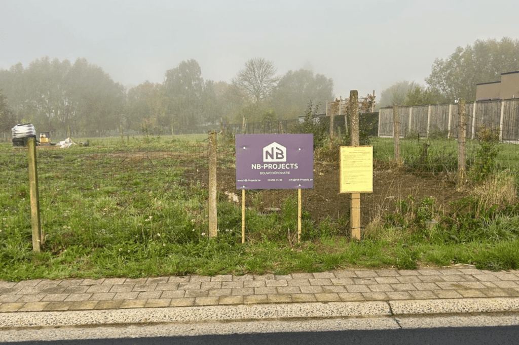 Lege bouwgrond met het NB-Projects bouwcoördinatie bord en de stedenbouwkundige vergunning.
