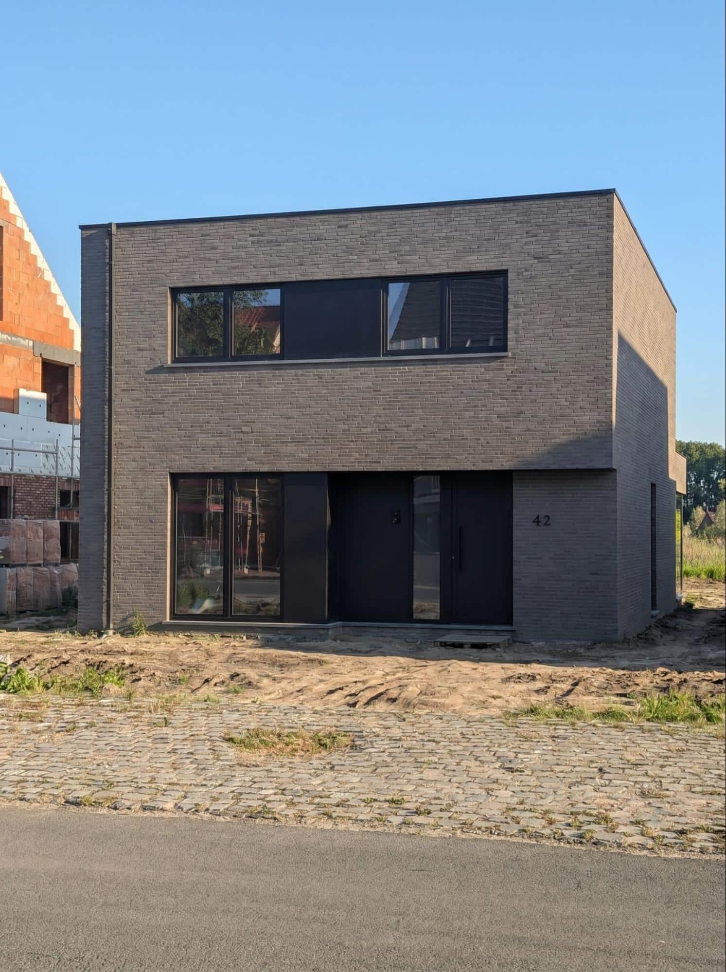 Moderne nieuwbouwwoning met grijsbruine gevelsteen en zwart schrijnwerk, gerealiseerd door NB-Projects