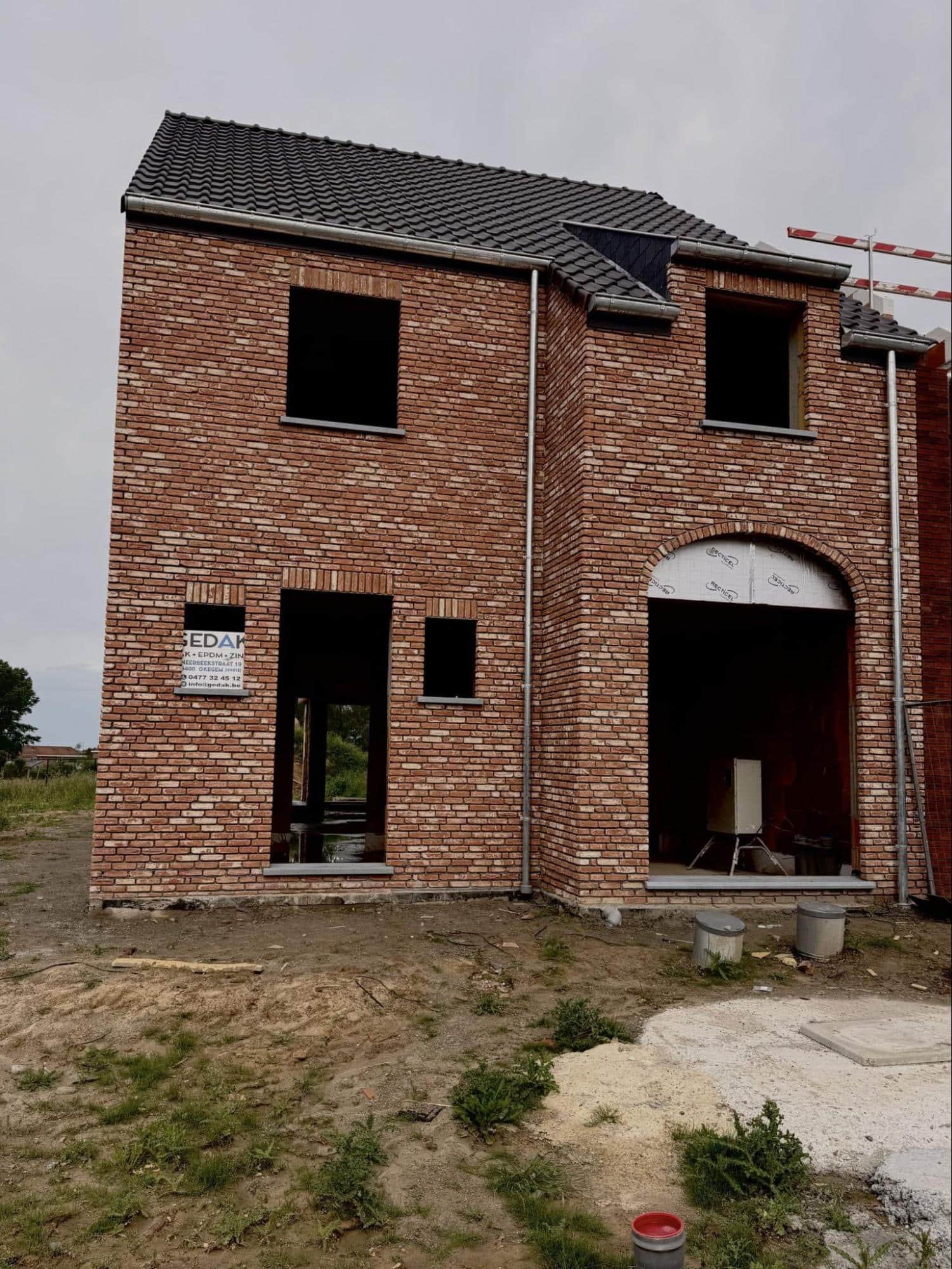 Ruwbouw van een nieuwbouwwoning in baksteen met dakpannen en nog te plaatsen ramen en deuren.
