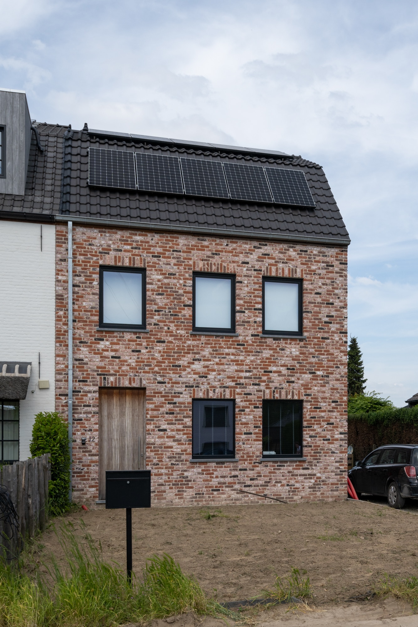 Halfopen bebouwing met bakstenen gevel, zwarte dakpannen en zonnepanelen op het hellend dak