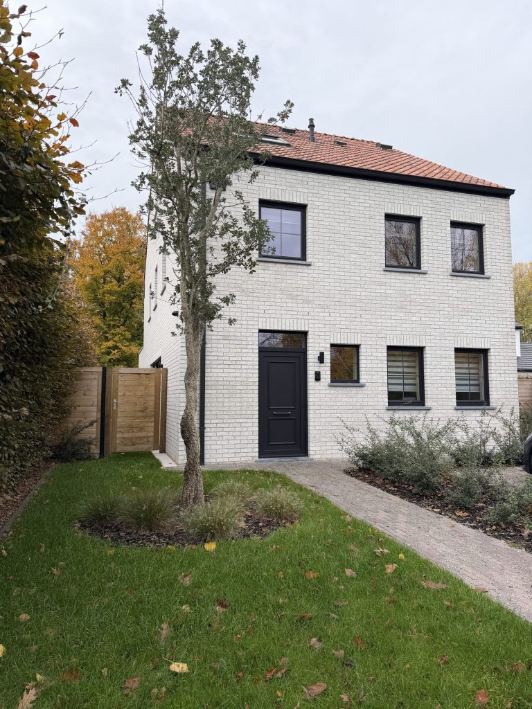 Witte landelijke woning met zwarte voordeur en tuin met boom