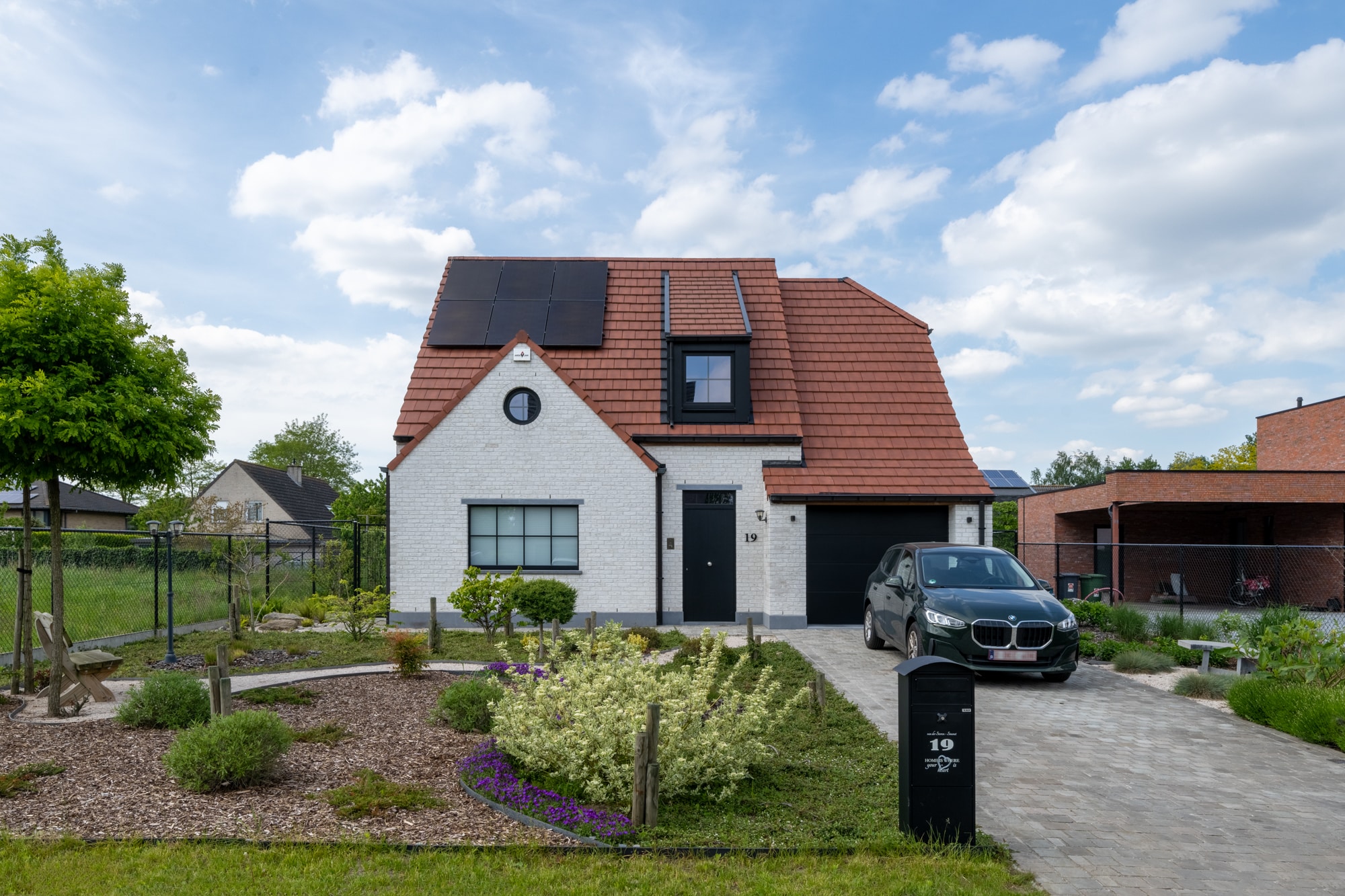 Klassieke sleutel-op-de-deur woning in witte gevelsteen met rood pannendak, zonnepanelen en een verzorgde voortuin.
